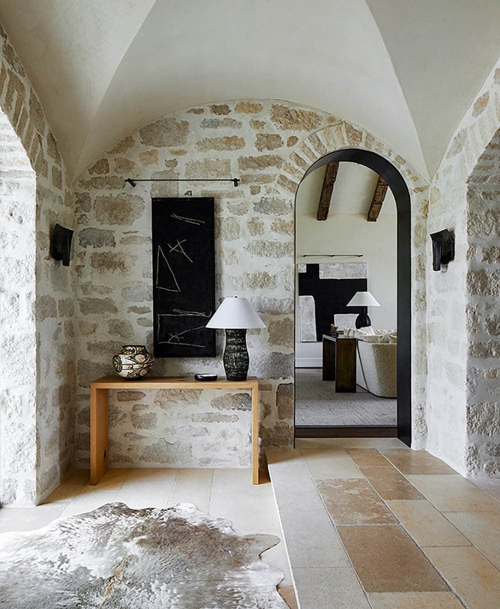 Stone archway entry hall with wooden console table, cowhide rug, and abstract black artwork