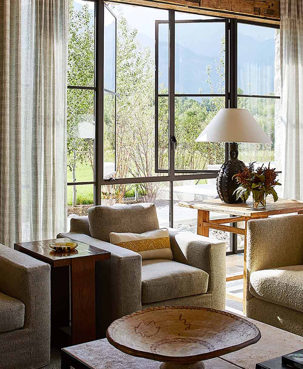 Boucle armchairs facing floor-to-ceiling steel-frame windows with mountain views