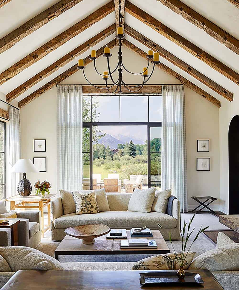 Vaulted living room with reclaimed wood beams, iron chandelier, and mountain views through glass doors