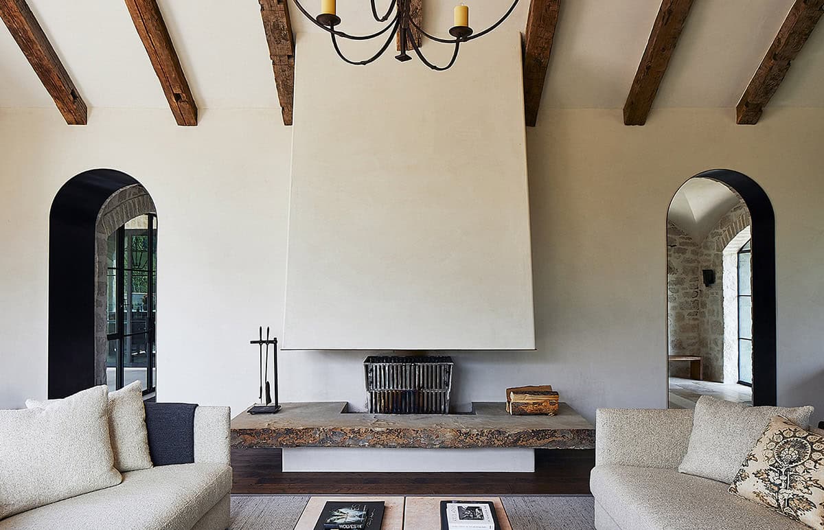 Minimalist plaster fireplace flanked by black arched doorways and reclaimed ceiling beams