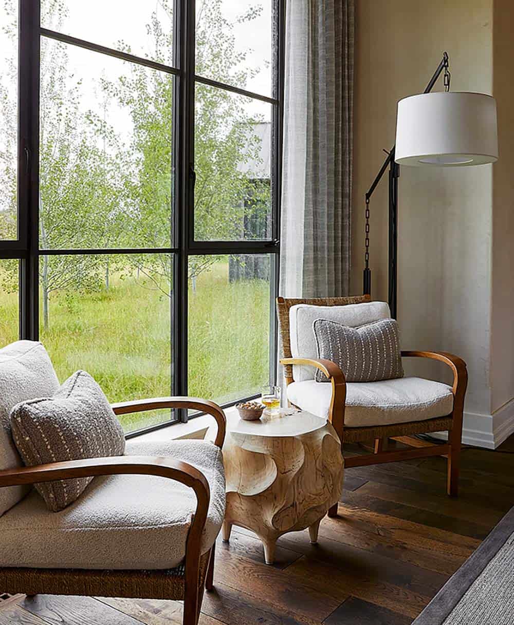 Pair of rattan-arm boucle chairs beside floor-to-ceiling windows overlooking meadow