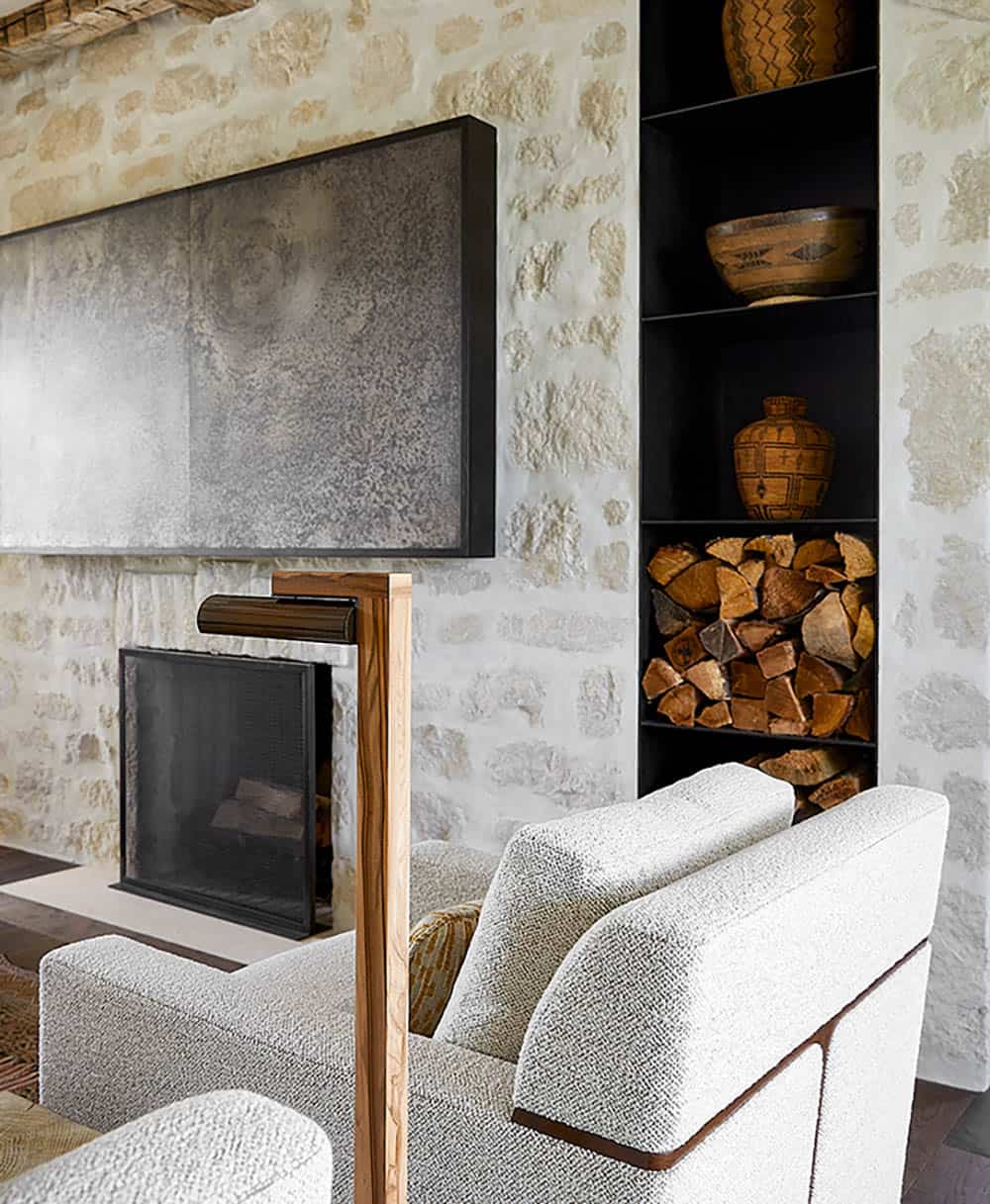 Fireplace detail with textured artwork, built-in firewood storage, and patterned pottery