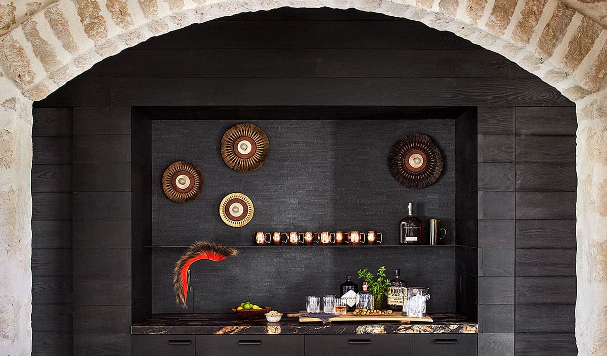 Dark wood bar niche with stone arch surround, decorative woven wall discs, and spirits display