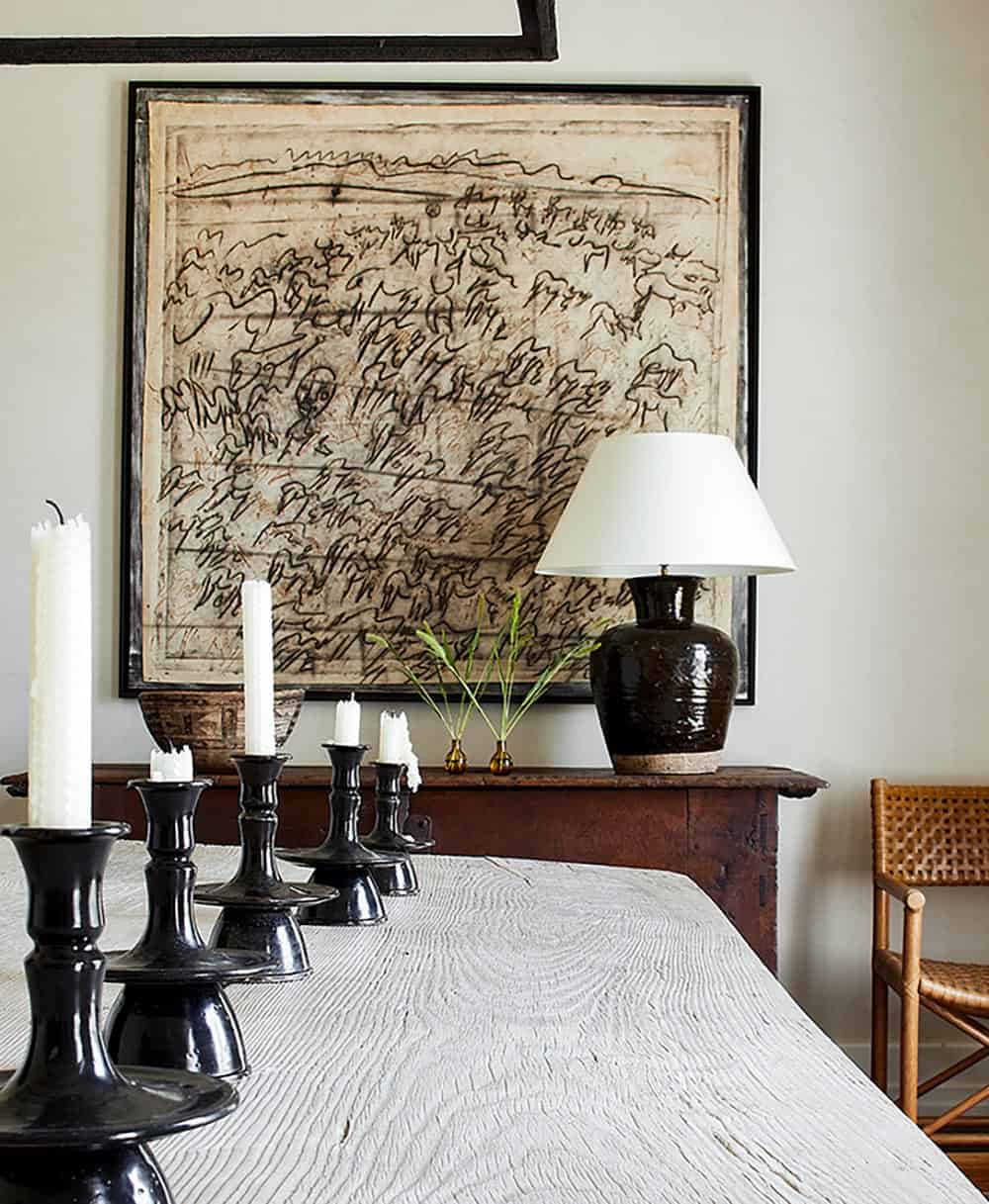 Dining vignette with expressive black ink artwork, dark ceramic lamp, and black candlesticks