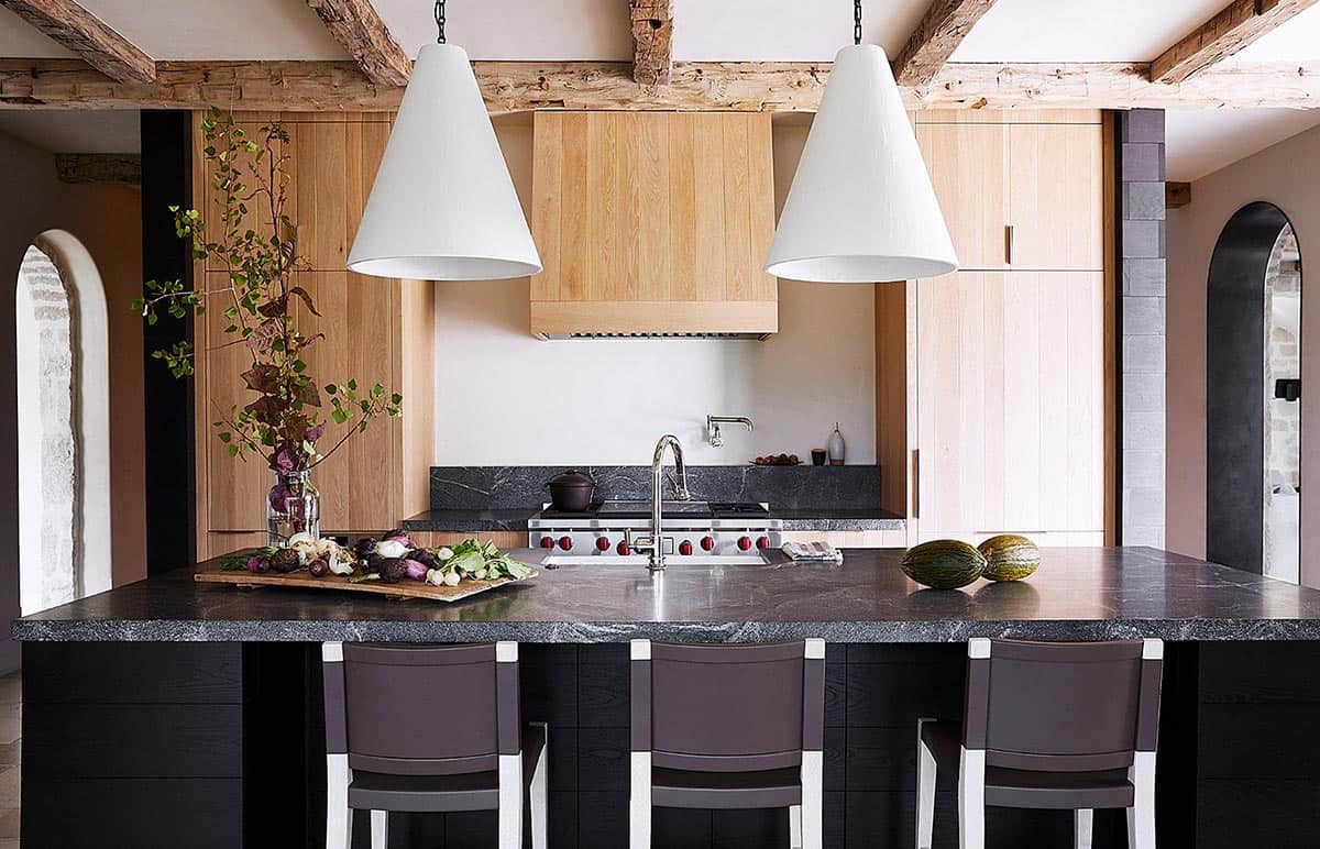 Kitchen with soapstone island, light oak cabinetry, reclaimed beams, and white cone pendants