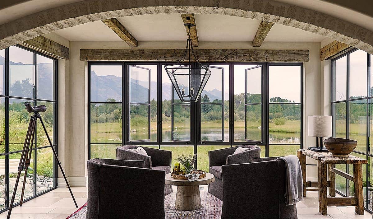 Glass-wrapped sitting room with stone arch, mountain and pond views, and lantern pendant