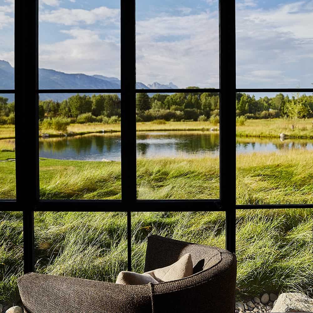 Floor-to-ceiling steel window framing wetland, pond, and mountain panorama
