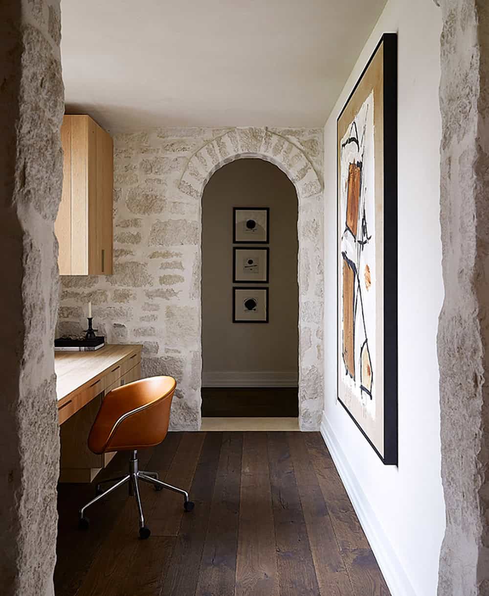 Compact home office with stone walls, light oak desk, leather chair, and arched alcove