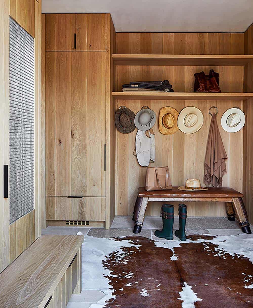Oak-paneled mudroom with cowhide rug, leather bench, cowboy hat hooks, and riding boots