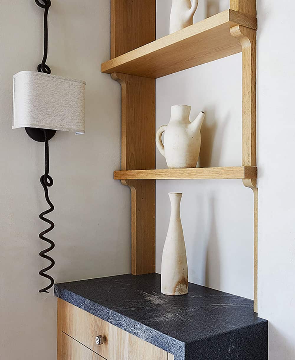 Close-up of oak ladder shelf with matte white stoneware pitchers and vase above soapstone counter