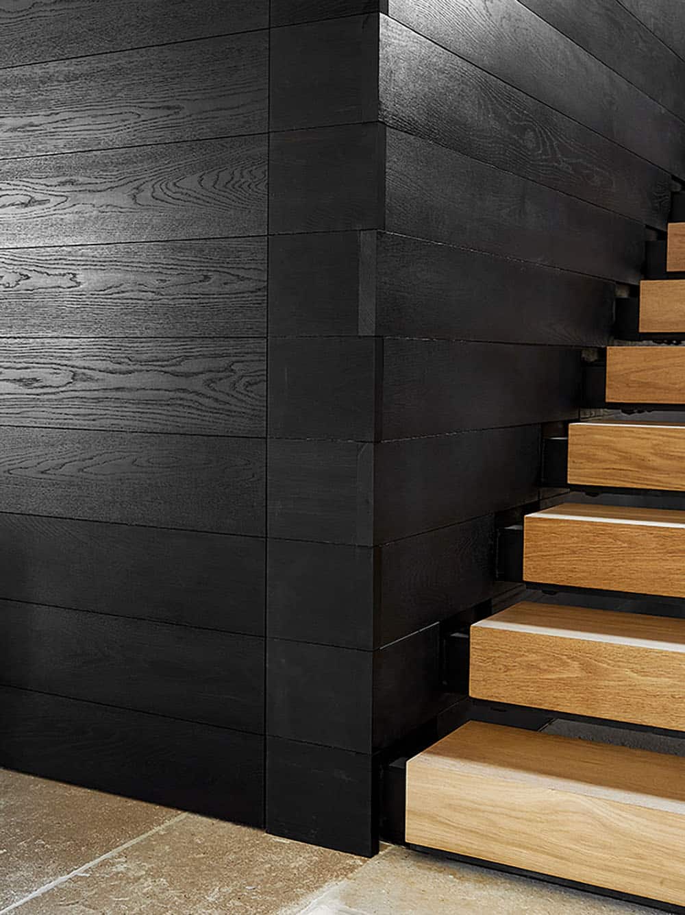 Close-up detail of natural oak stair treads cantilevered from charred black wood stringer wall