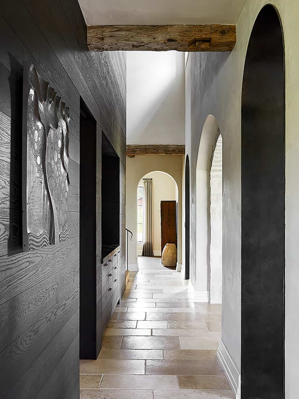Long hallway with charred wood paneling, stone arches, reclaimed beam ceiling, and sculptural wall art