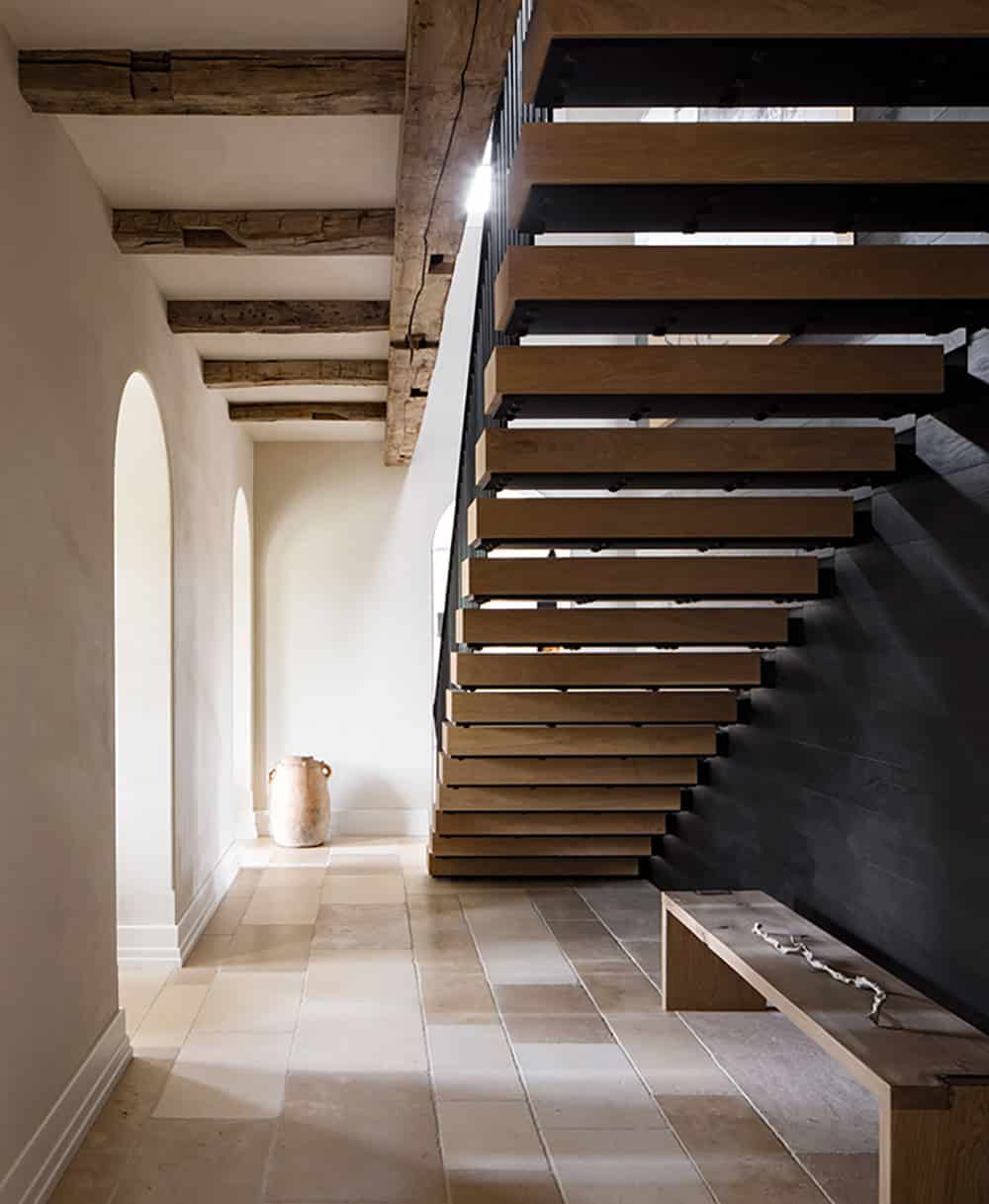 Floating oak stair treads on black steel stringer beside arched plaster hallway with terracotta urn