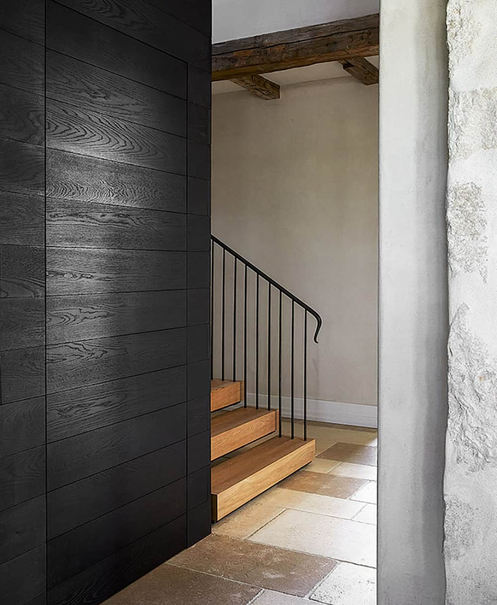 Oak stair treads with iron balustrade and curved handrail beside charred wood panel wall