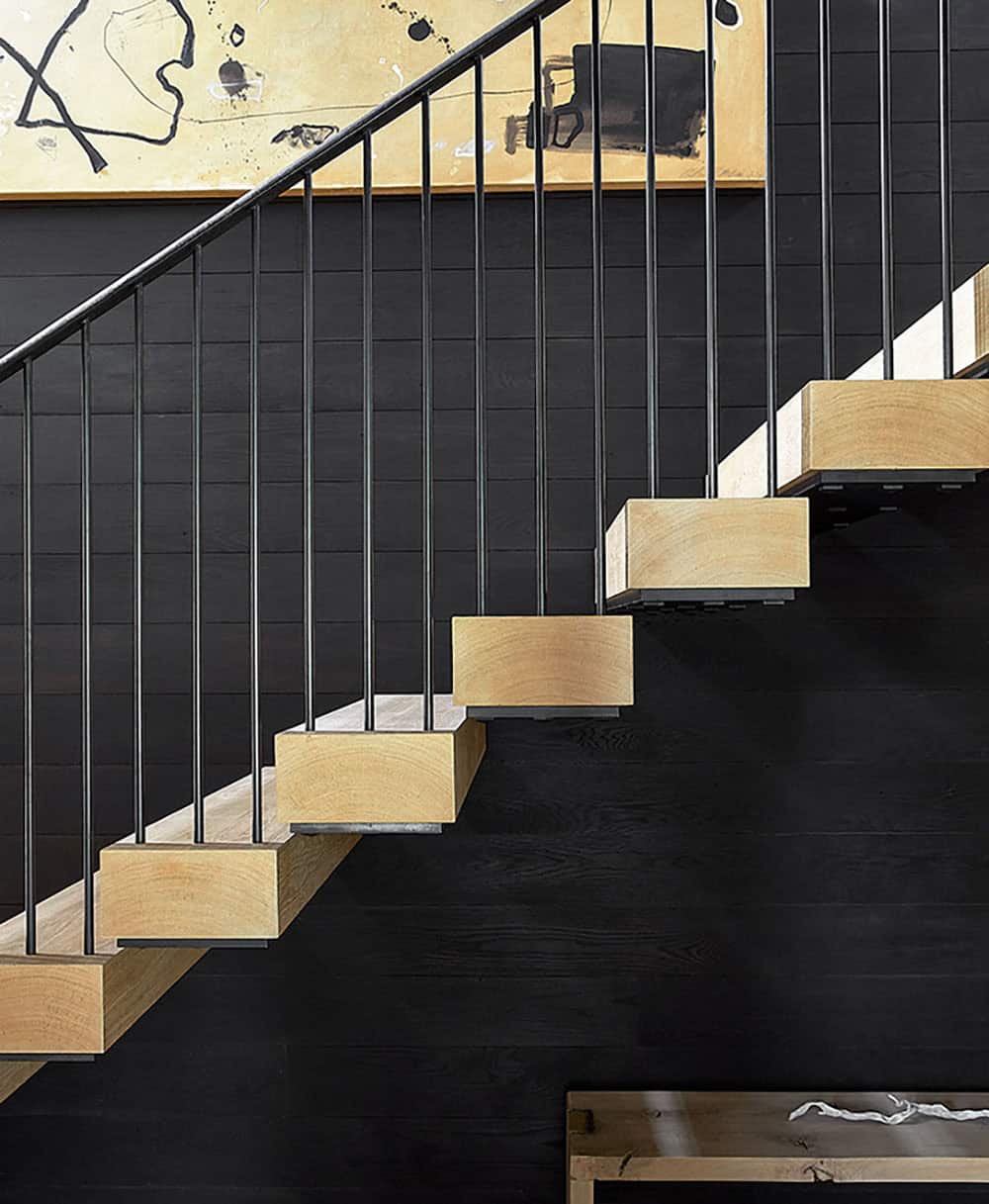 Close-up of floating oak stair treads against charred black wood paneling with abstract artwork above