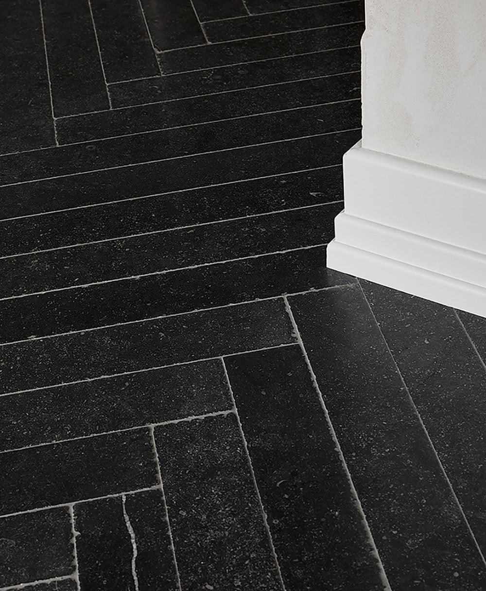 Close-up detail of black herringbone stone tile floor against white plaster baseboard