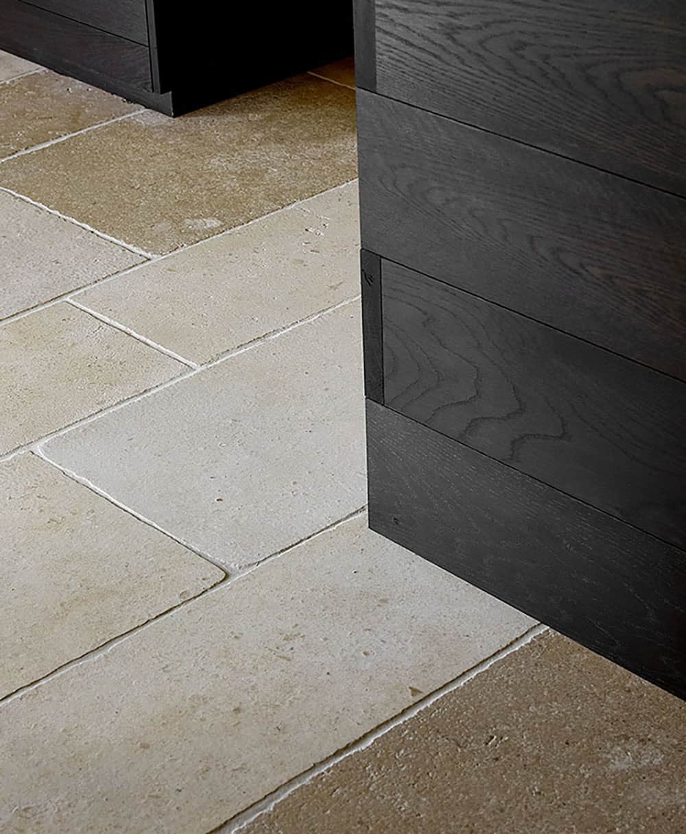 Detail of antique limestone floor tiles meeting charred black oak wall paneling