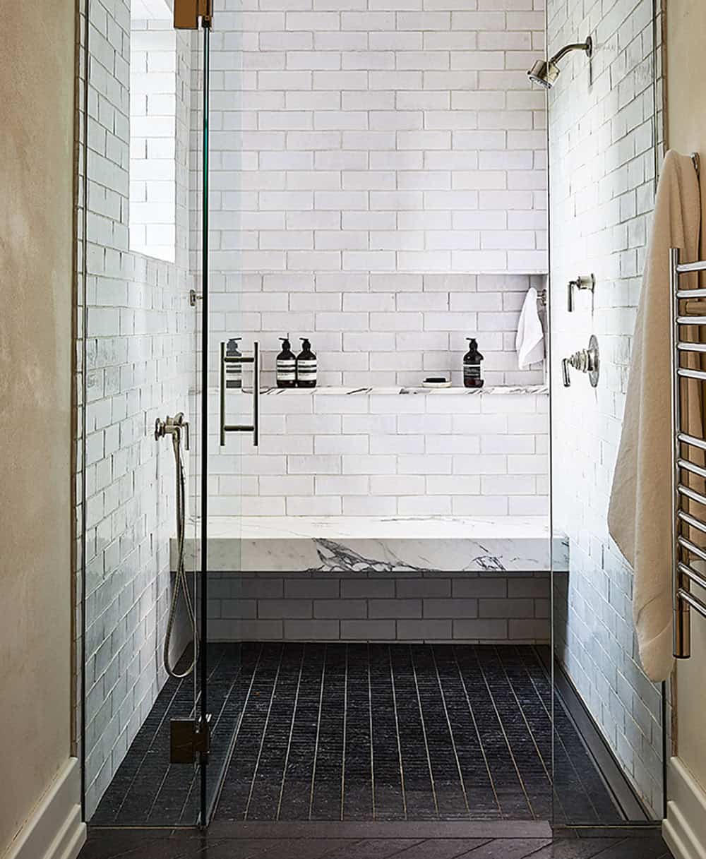 Walk-in shower with white subway tile, marble bench, dark stone floor, and glass enclosure