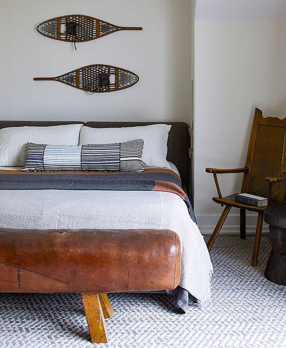 Guest bedroom with vintage snowshoe wall art, leather pommel horse bench, and antique wooden chair