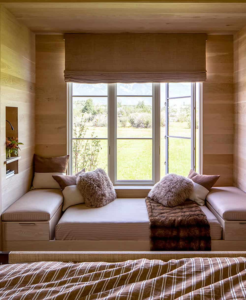 Wood-paneled bedroom window seat nook with fluffy pillows, fur throw, and Grand Teton mountain views