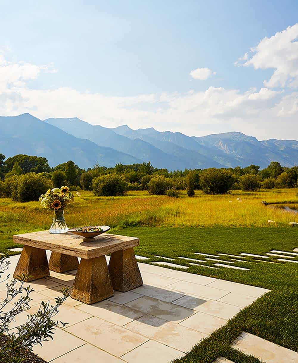 Stone patio with rustic stone pedestal table, sunflower arrangement, and sweeping Teton mountain views