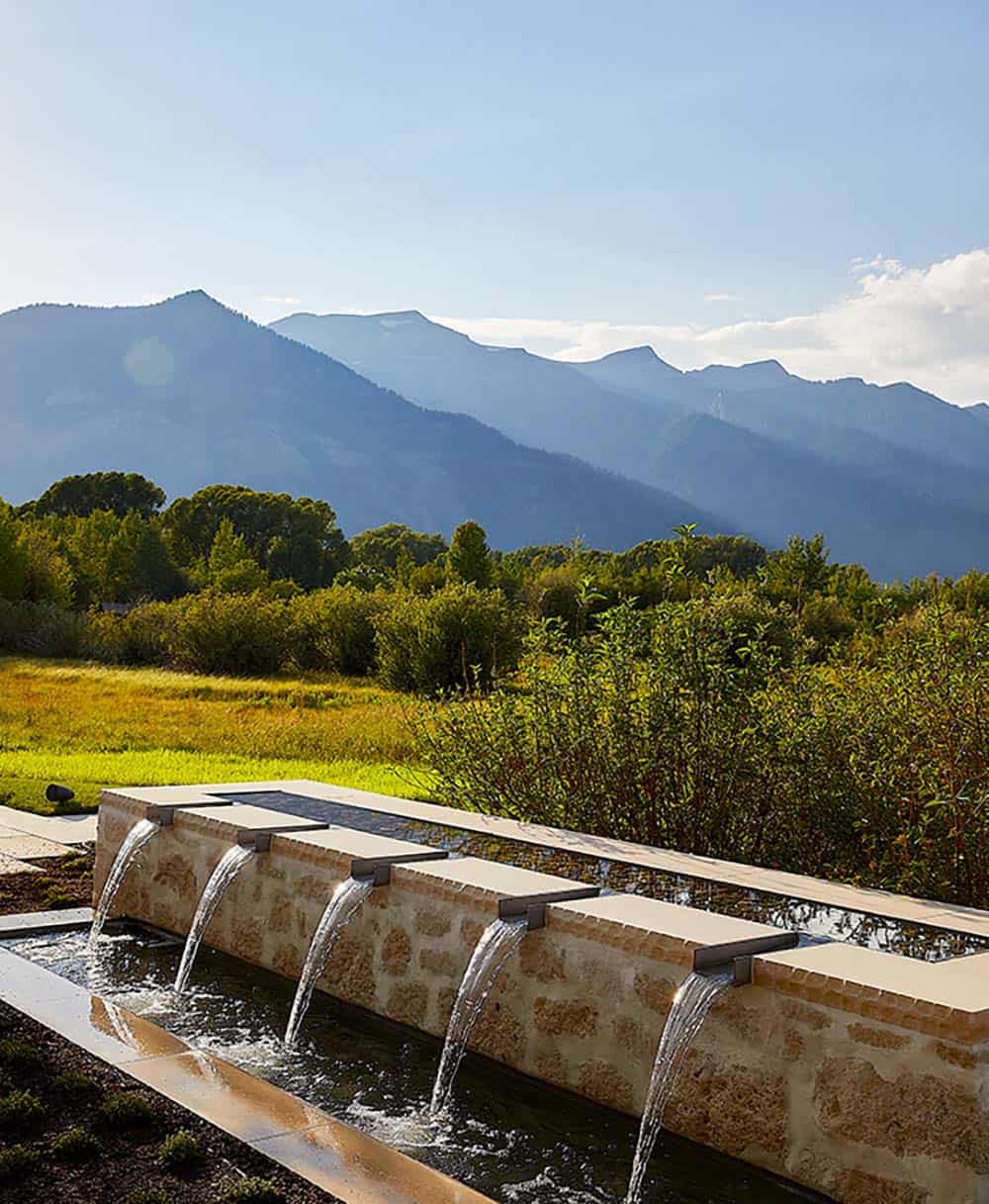 Linear stone water feature with multiple cascading spouts and panoramic Wyoming mountain backdrop