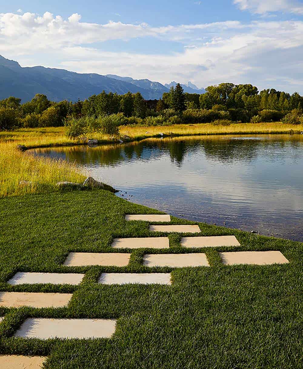 Geometric limestone stepping stones set in manicured grass leading to natural pond with Teton views