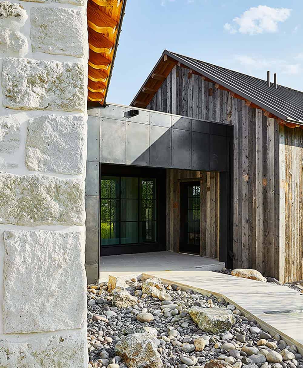 Exterior entry detail with stone wall, weathered board-and-batten siding, metal panels, and river rock landscaping