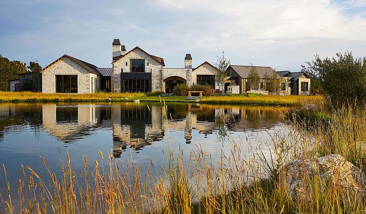 Full exterior view of stone and reclaimed wood mountain home reflected in natural pond at golden hour