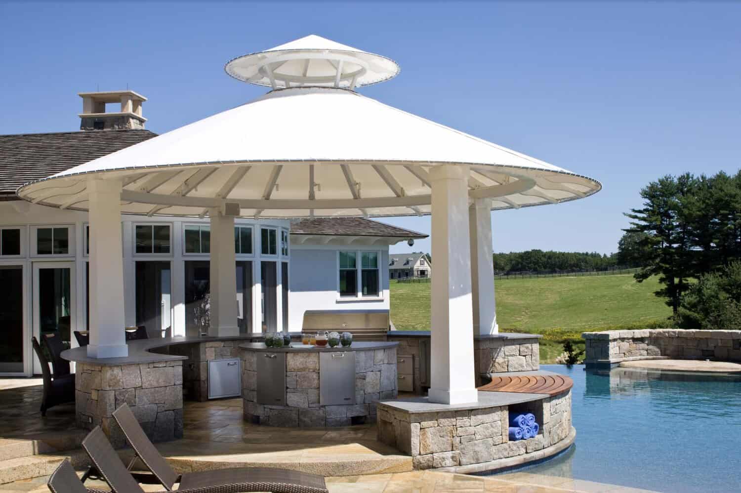 Outdoor Kitchen Under White Circular Gazebo With Stone Bar and Poolside Seating