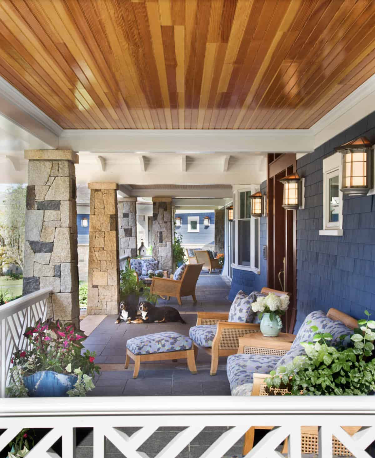 Wraparound Porch With Cedar Ceiling, Stone Columns, and Blue Floral Wicker Seating