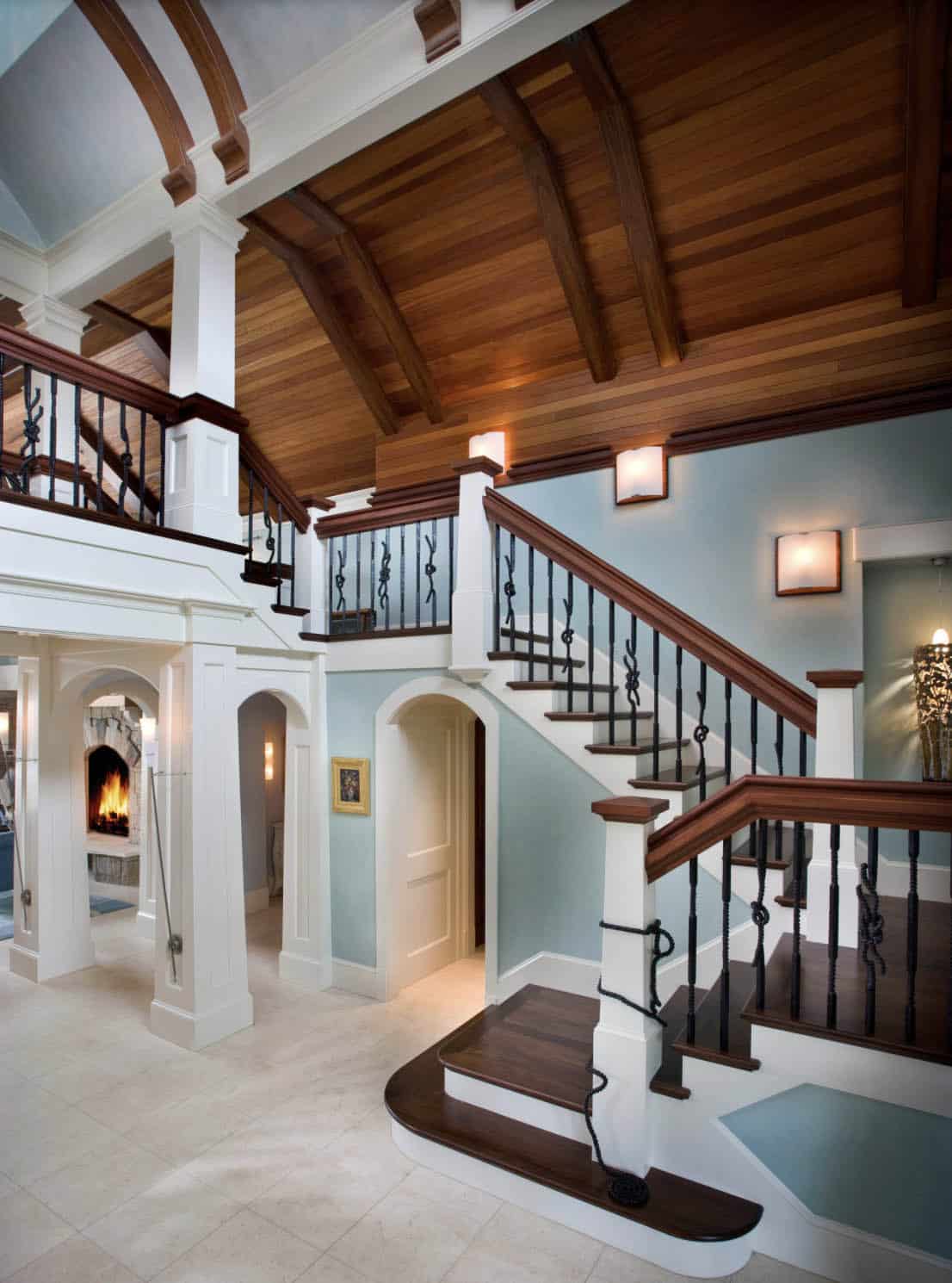 Grand Foyer Staircase With Wood Ceiling, Iron Rope Balusters, and Arched Fireplace Nook