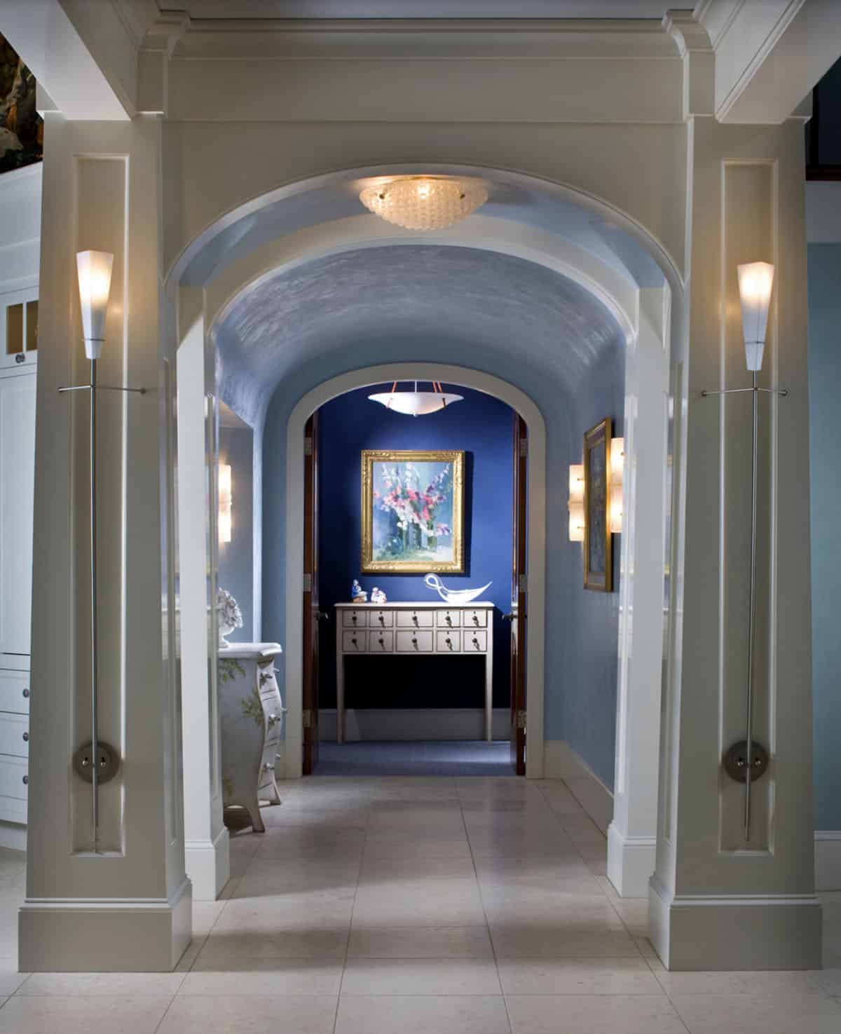 Barrel Vaulted Hallway With Arched Entry, Torchiere Sconces, and Navy Blue Accent Wall