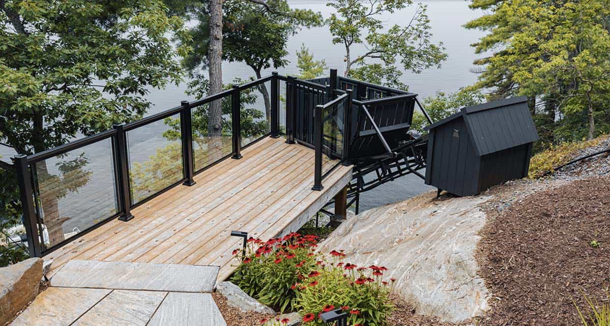 Waterfront cedar deck with black glass railing, red coneflowers, and funicular rail system