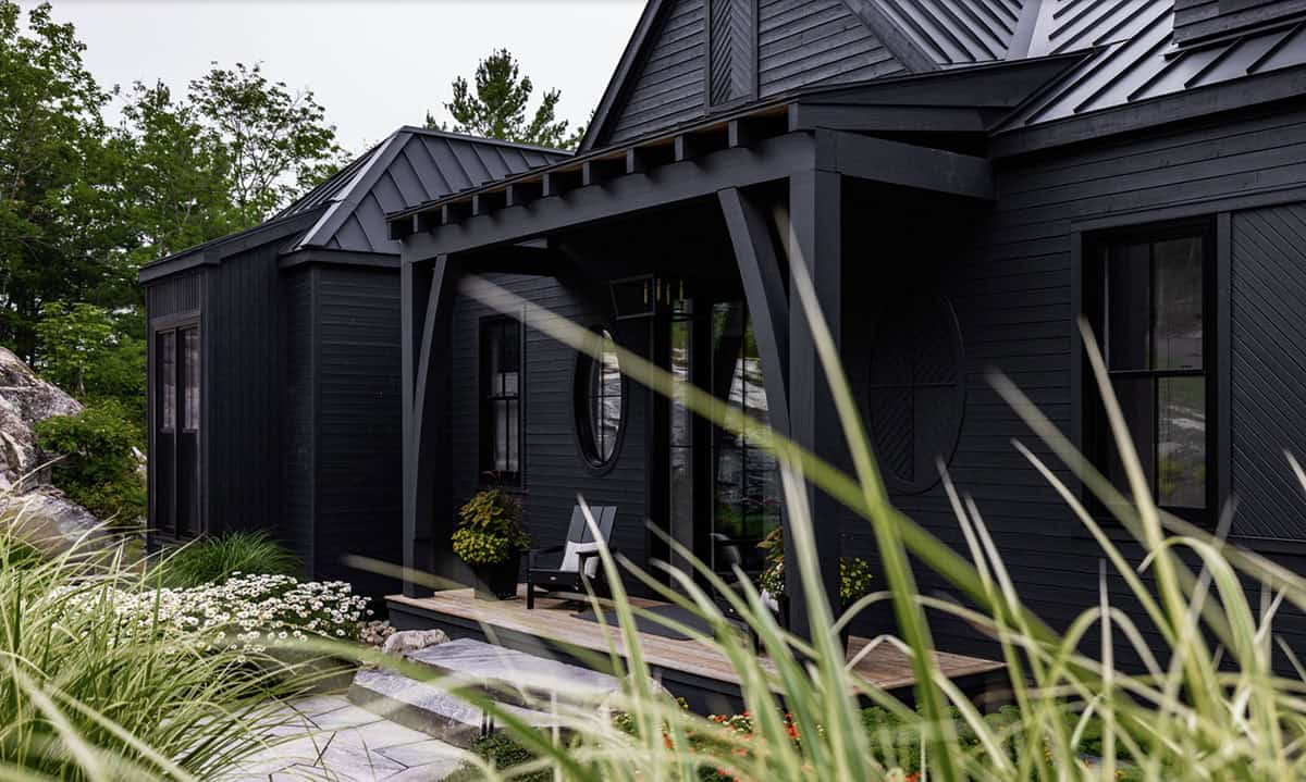 Black cottage front porch with decorative circular wood panel and ornamental grasses in foreground