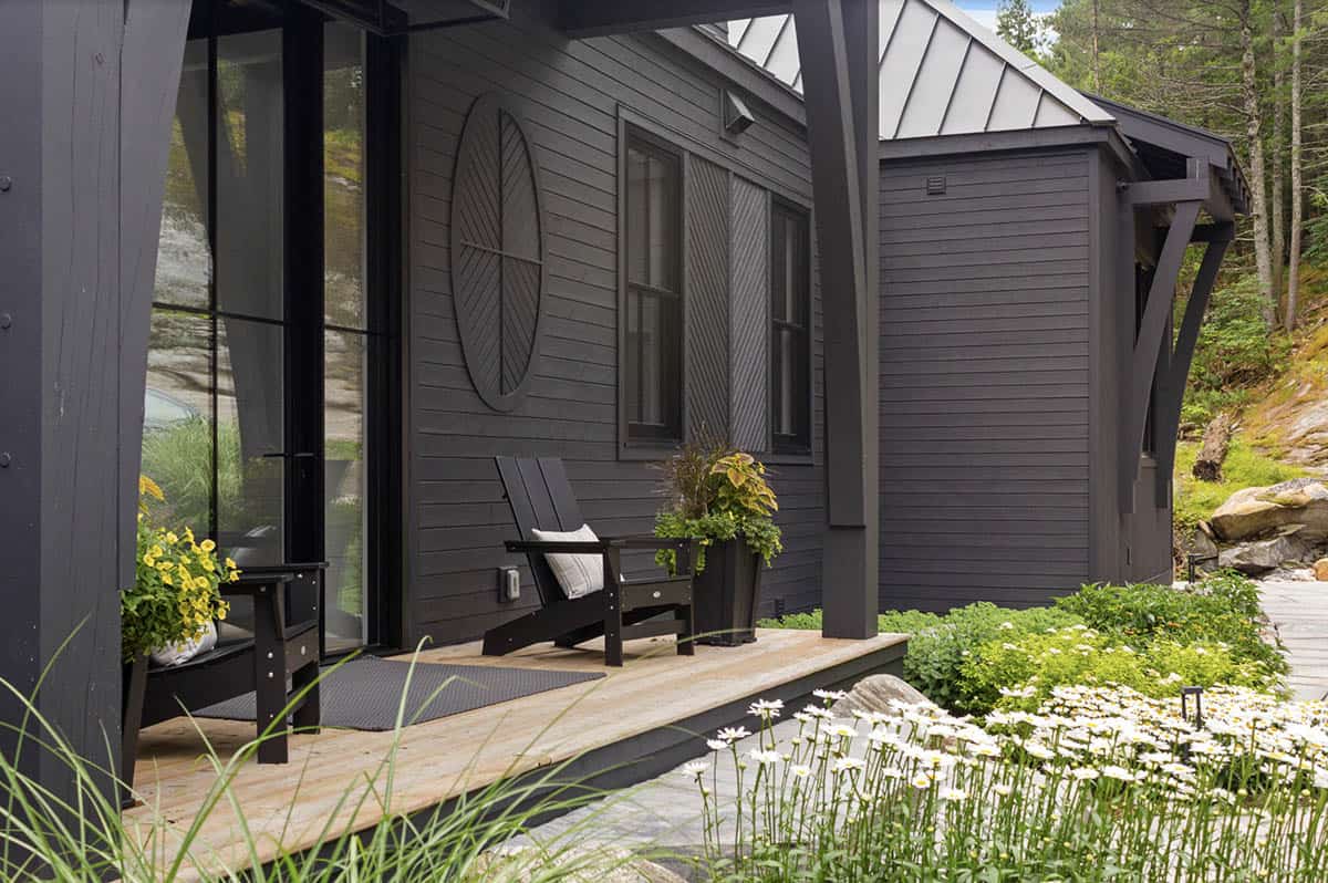Dark cottage entry porch with Adirondack chairs, circular wood wall medallion, and daisy garden