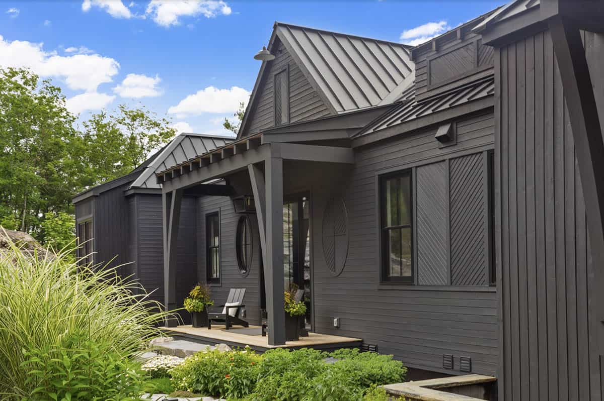 Charcoal cottage exterior with standing seam metal roof, decorative siding patterns, and lush landscaping