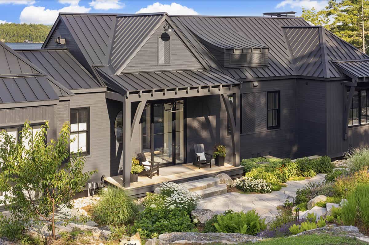 Charcoal cottage with arched porch brackets, standing seam roof, and manicured perennial garden