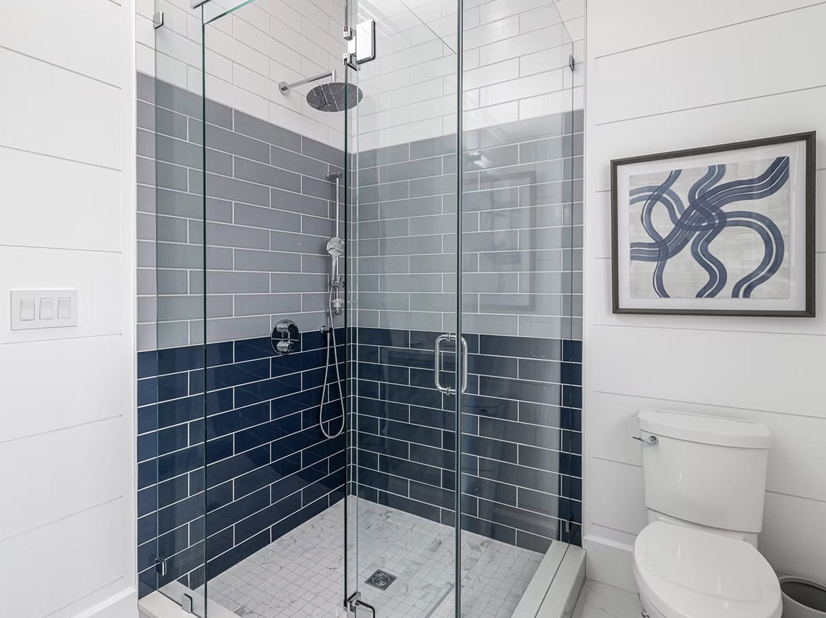 Boathouse shower with ombre navy-to-gray subway tile, glass enclosure, and marble mosaic floor