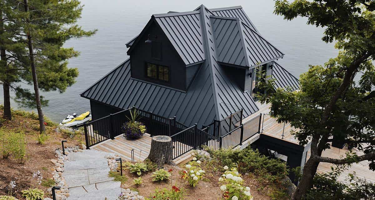 Aerial view of black boathouse with standing-seam metal roof, wrap-around deck, and jet ski