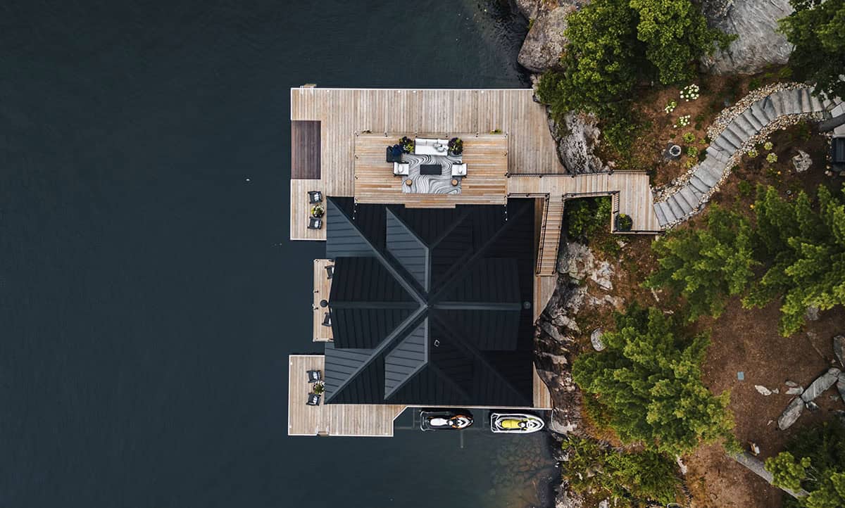  Overhead drone view of boathouse rooftop, surrounding cedar decks, and jet skis at water entry