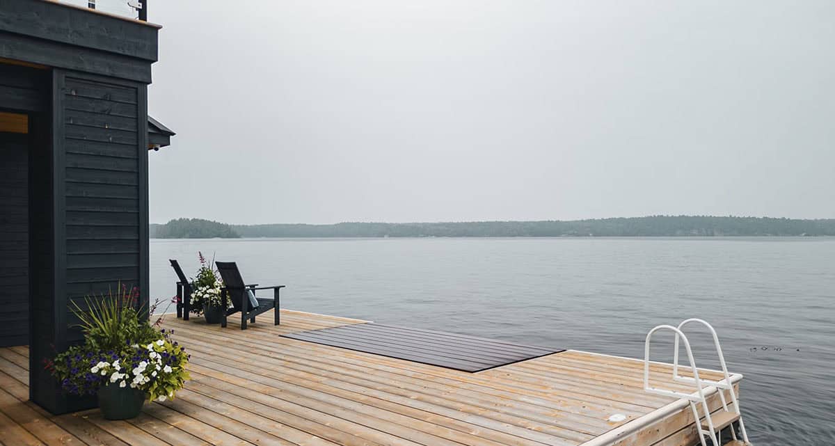 Cedar dock beside black boathouse with Adirondack chairs and lake views on a misty day