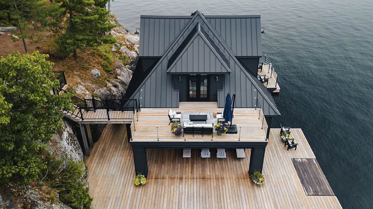 Aerial view of boathouse upper deck with outdoor sofa seating, patio umbrella, and glass railings overlooking the lake