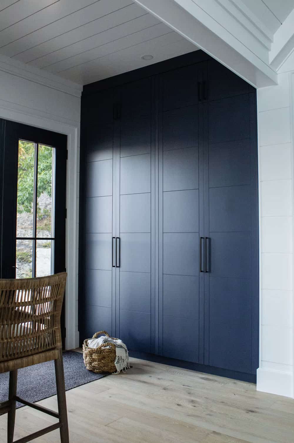 Floor-to-ceiling navy blue built-in storage cabinets with black hardware in boathouse entryway