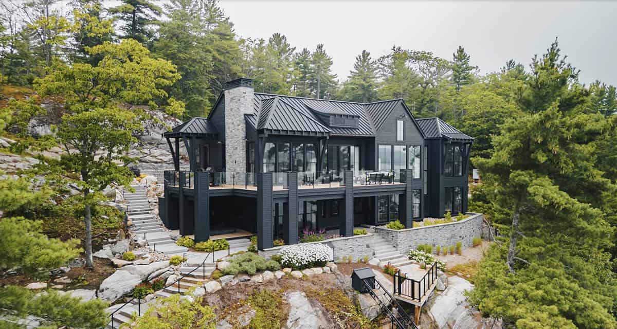 Aerial view of black two-story lake cottage with large glass facade and funicular below