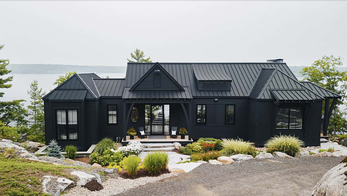Front aerial of black cottage with symmetrical gabled roof and oval window above entry porch