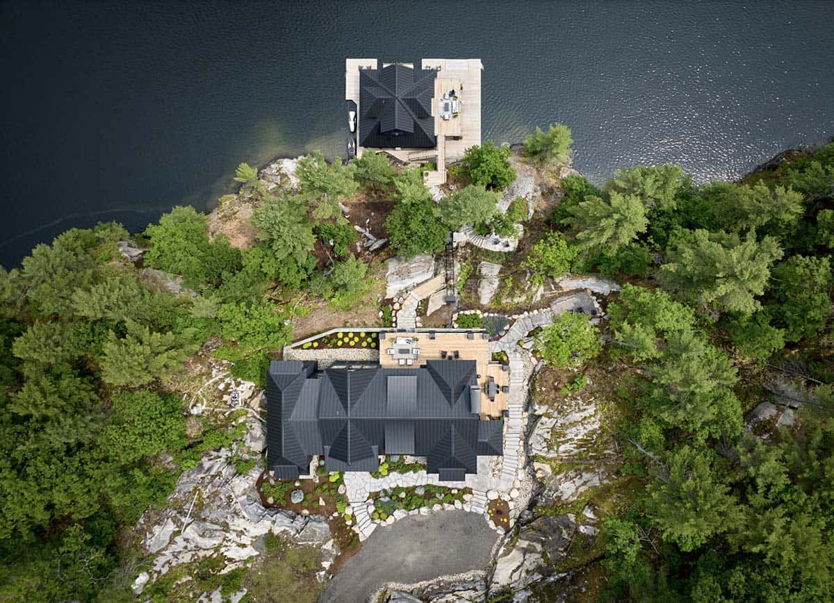 Straight-down aerial of rocky peninsula showing cottage roof and matching black boathouse on water