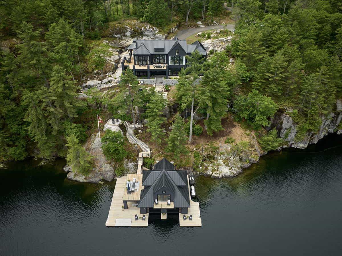 Wide aerial of dark cottage on rocky point with matching black boathouse and timber dock