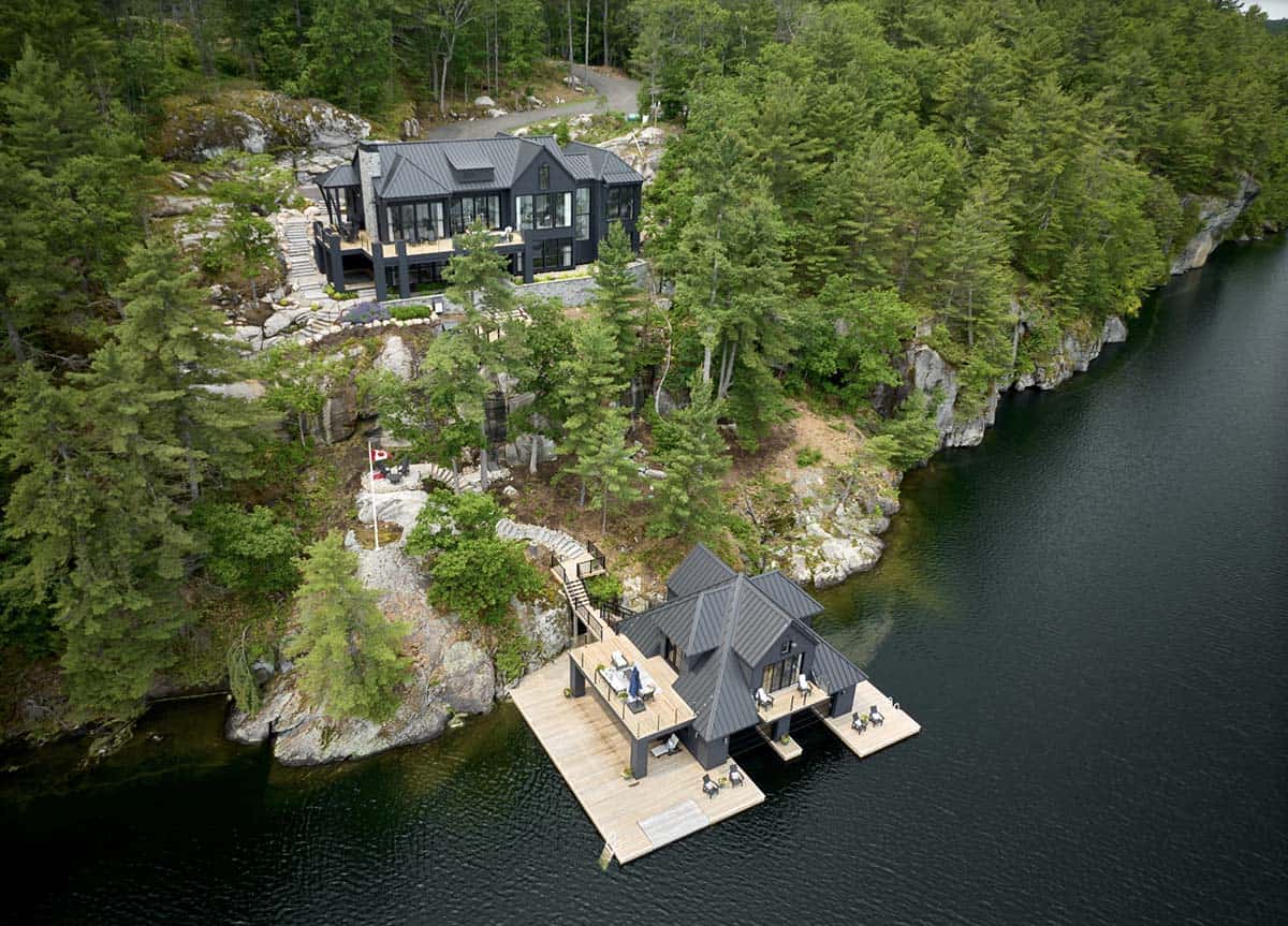 Aerial view of dark cottage and matching boathouse with timber dock on rocky Canadian Shield lakefront