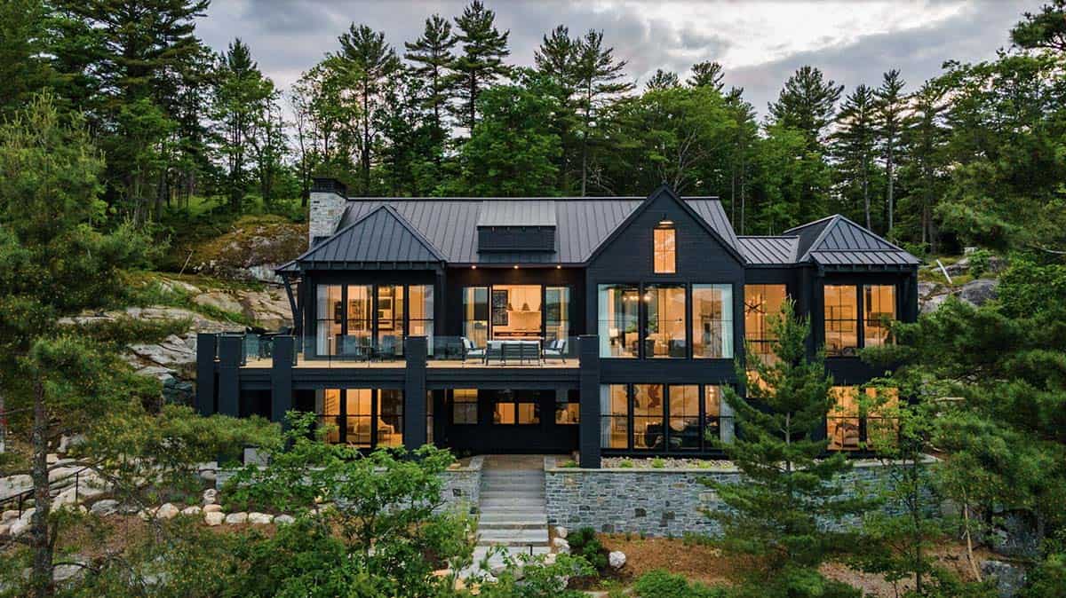 Dusk exterior of dark cottage with warmly lit interiors visible through floor-to-ceiling windows